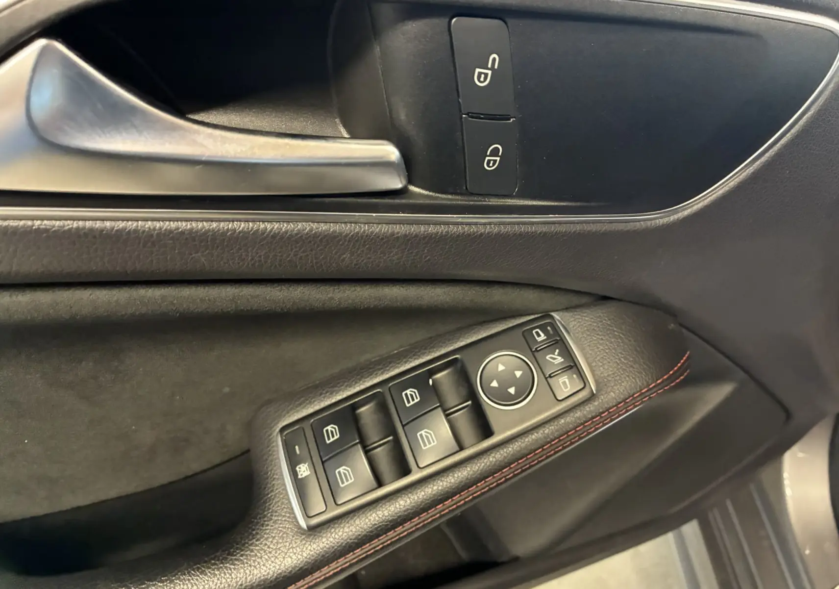 Gros plan sur la porte côté gauche d'une Mercedes Classe A 250 AMG Sport gris, avec commandes électriques et surpiqûres rouges.