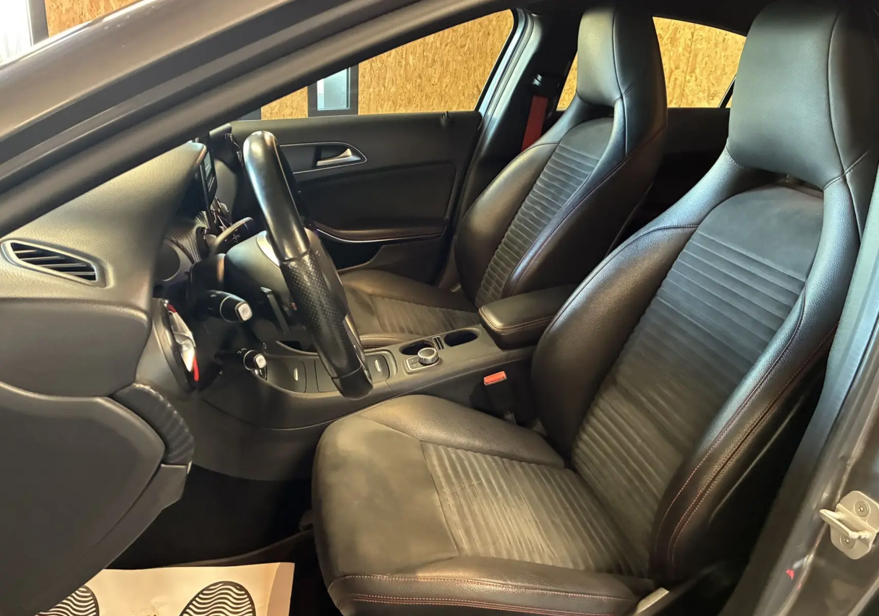 Vue intérieure côté conducteur de la Mercedes Classe A 250 AMG Sport 2014 avec sièges en cuir noir et volant sport.