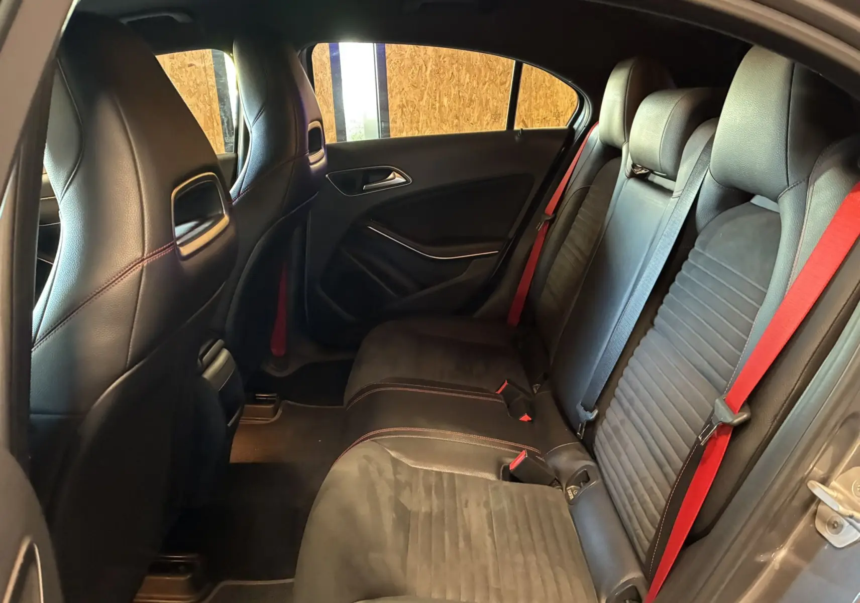 Vue intérieure arrière côté droit de la Mercedes Classe A 250 AMG Sport 2014 avec sièges noirs et ceintures rouges.