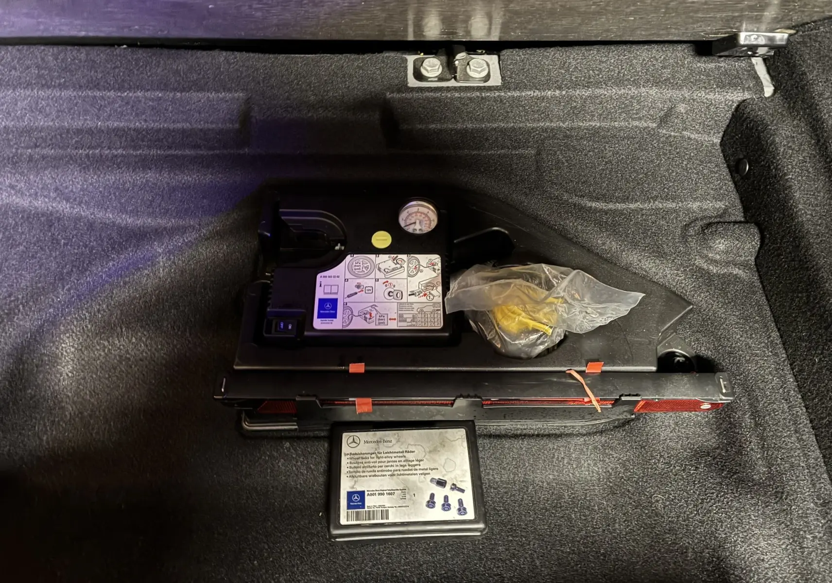 Gros plan sur le compresseur et kit de réparation de pneu dans le coffre d'une Mercedes Classe A 250 AMG Sport gris.