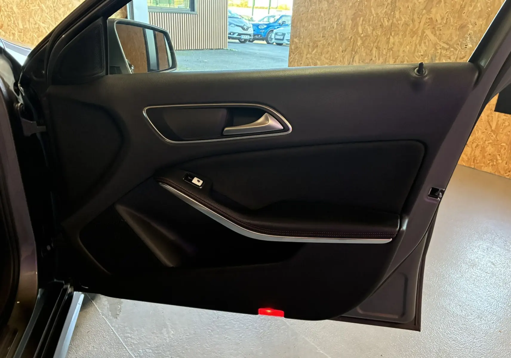 Vue intérieure de la porte avant gauche noire d'une Mercedes Classe A 250 AMG Sport gris, avec poignée argentée et bouton de fenêtre.