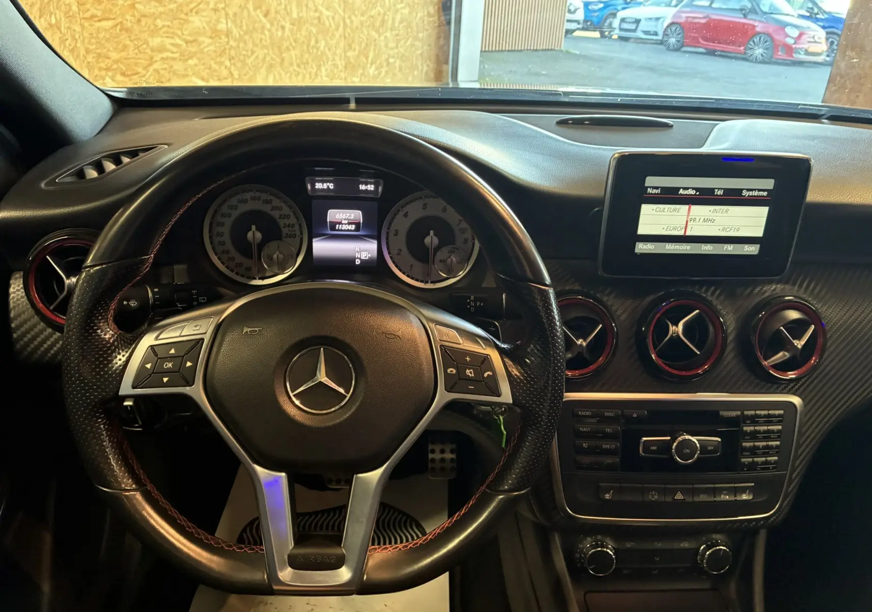 Vue intérieure du tableau de bord d'une Mercedes Classe A 250 AMG Sport 2014 avec volant cuir noir et écran central multimédia.