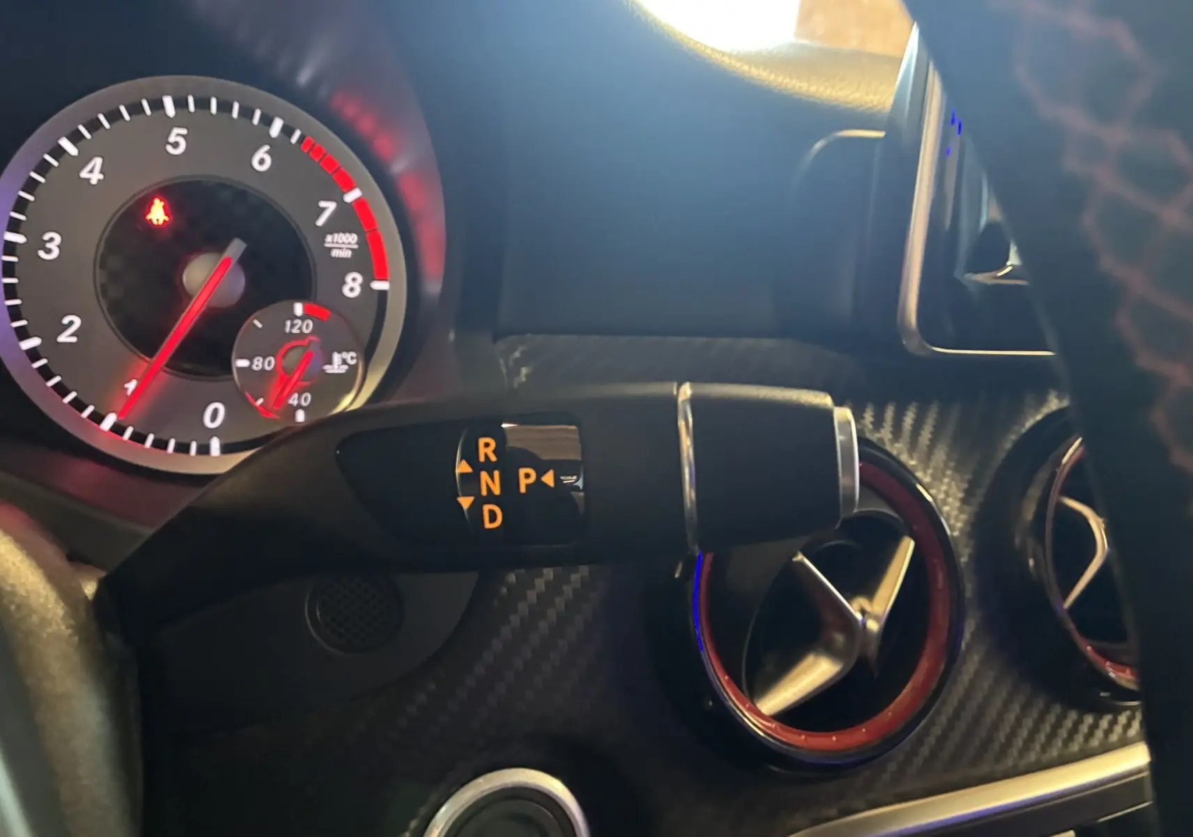 Gros plan intérieur sur le levier de vitesses automatique et les aérateurs rouges d'une Mercedes Classe A 250 AMG Sport gris.