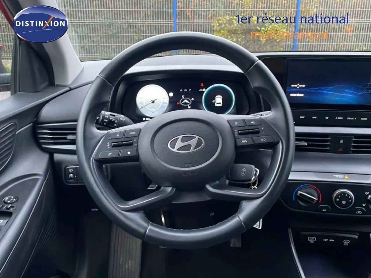 Vue intérieure centrée sur le volant cuir noir d'une Hyundai i20 2025 avec tableau de bord digital et écran tactile.