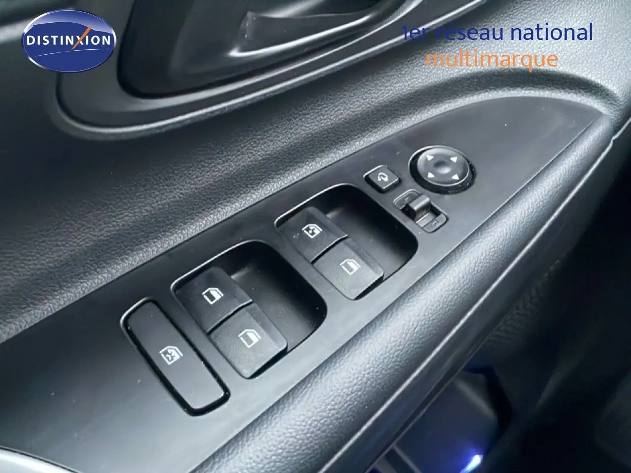 Gros plan sur les commandes des vitres électriques et rétroviseurs côté conducteur de la Hyundai i20 rouge Dragon Metal 2025.