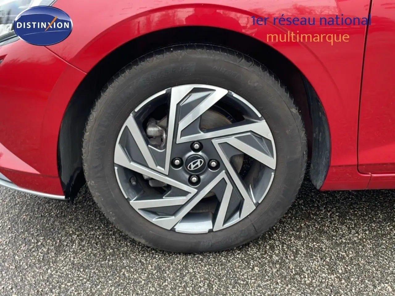 Gros plan sur la roue avant gauche d'une Hyundai i20 rouge Dragon Metal avec jante alliage au design géométrique.