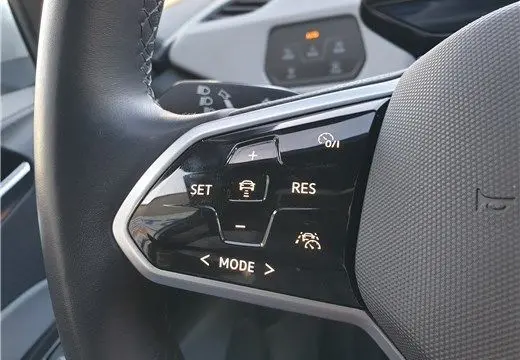 Gros plan sur les commandes au volant noir du Volkswagen ID.3 blanc glacier, mettant en valeur les fonctions d'aide à la conduite.