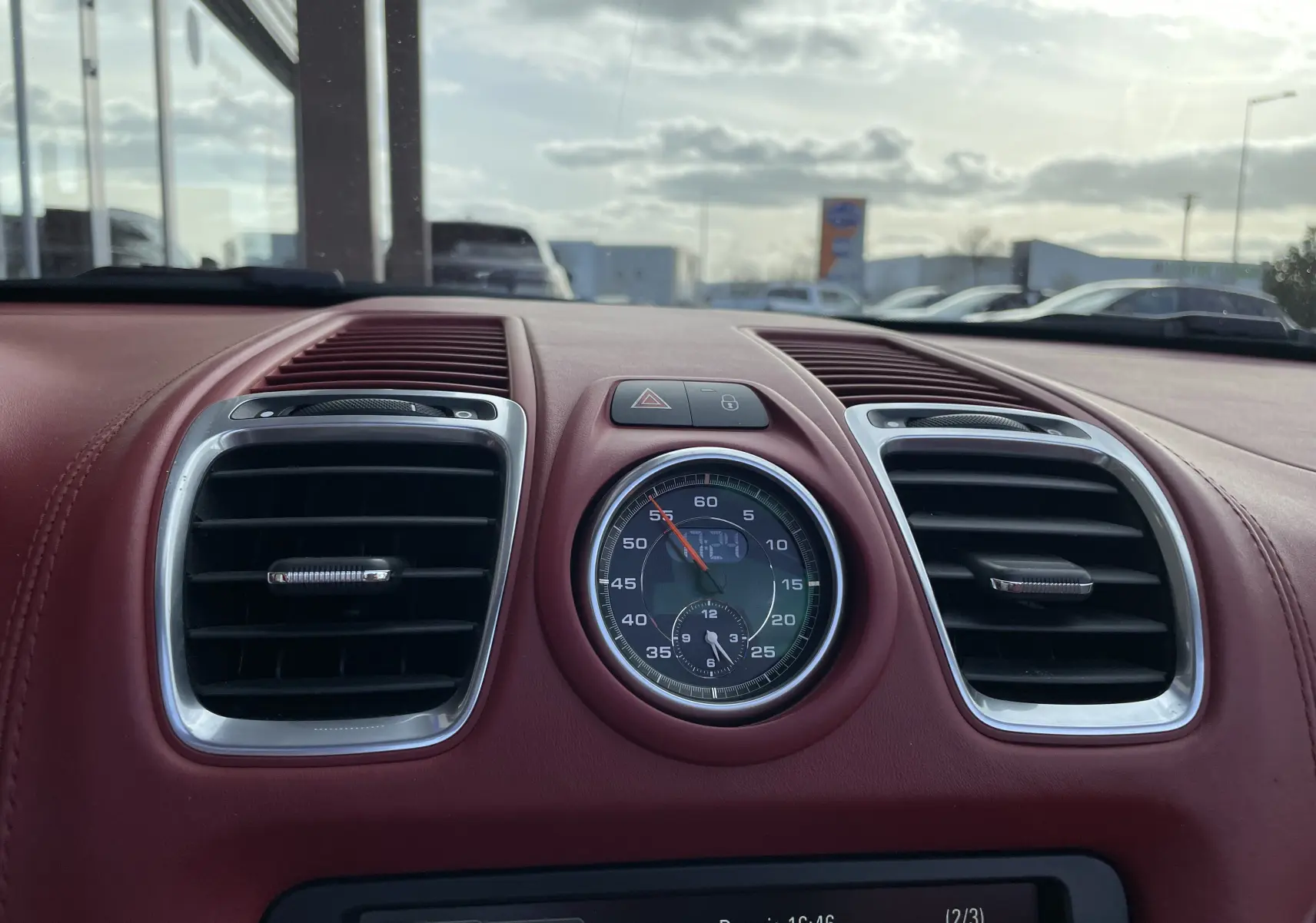 Gros plan sur le tableau de bord rouge grenat de la Porsche Boxster S 981 avec horloge centrale et aérateurs chromés.