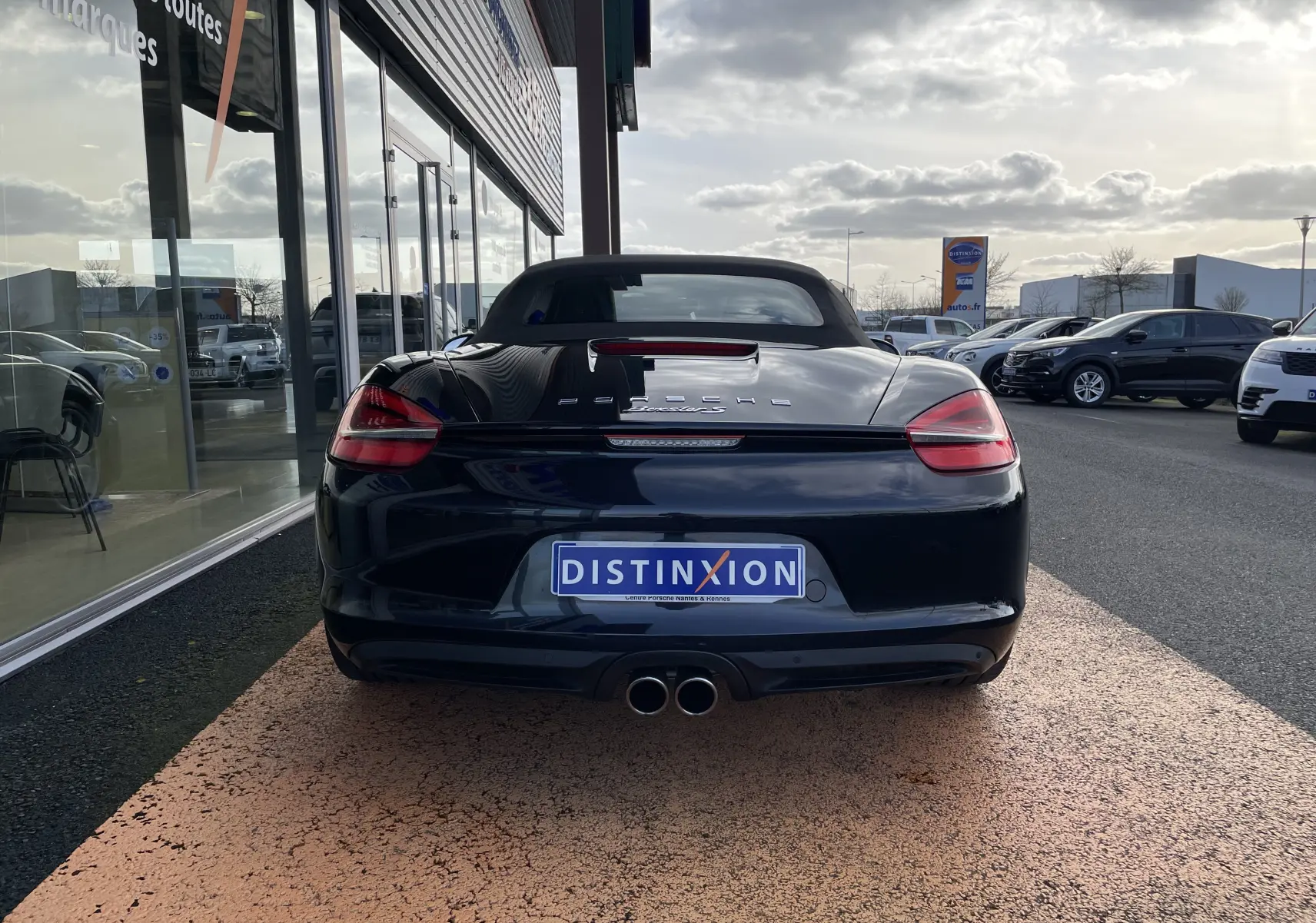 Vue arrière d'une Porsche Boxster S 981 noire intense avec capote noire et double sortie d'échappement centrale.