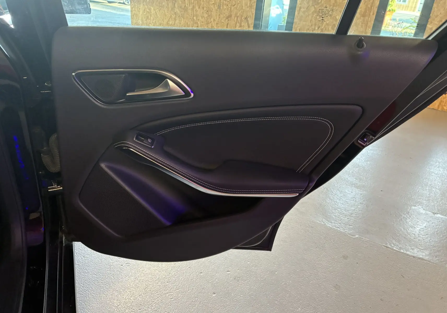 Gros plan sur la porte arrière gauche noire d'une Mercedes Classe A 180 CDI 2018, avec garniture cuir et surpiqûres blanches.