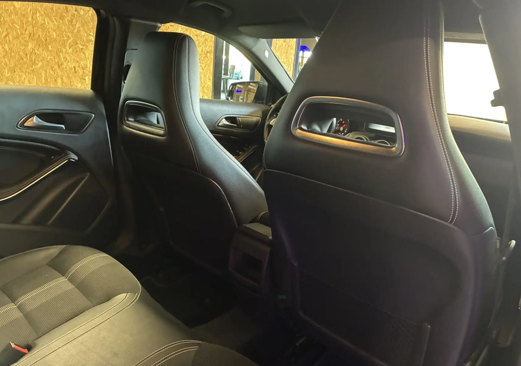 Vue intérieure arrière de la Mercedes Classe A 180 CDI noire, montrant les sièges avant en cuir noir avec surpiqûres blanches.