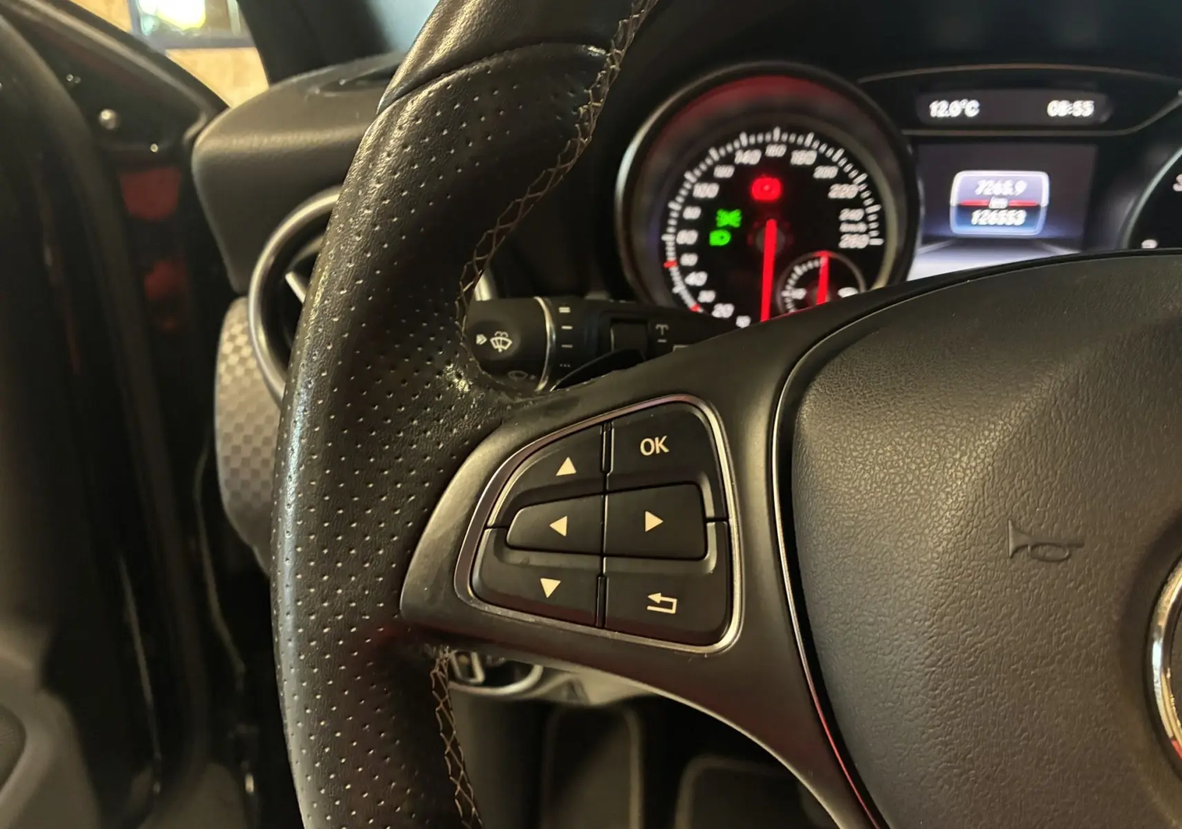 Gros plan sur le volant en cuir noir perforé et les commandes multifonctions à gauche du tableau de bord d'une Mercedes Classe A 180 CDI.