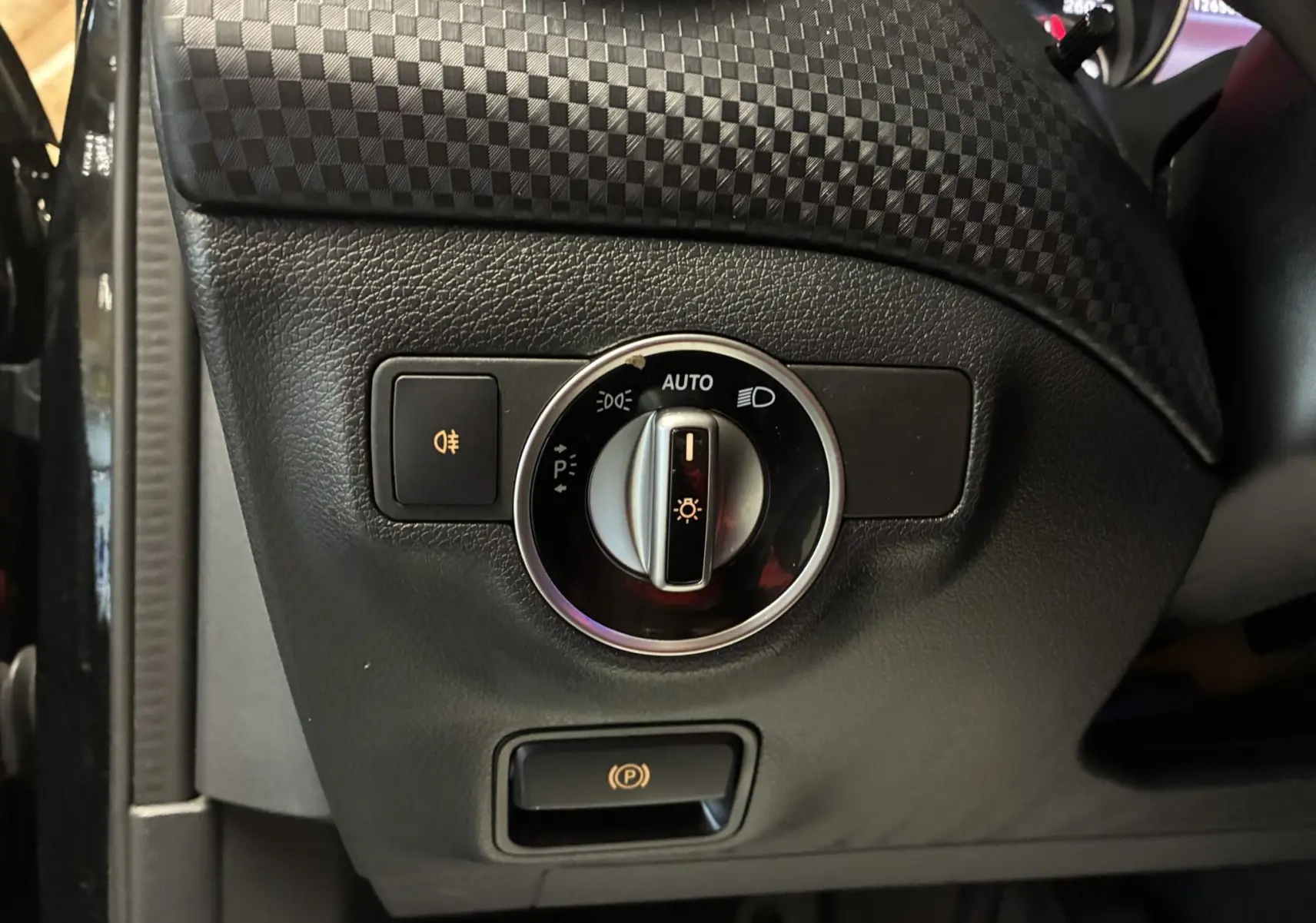 Gros plan sur le bouton de commande des phares et frein à main électrique dans une Mercedes Classe A 180 CDI noire de 2018.