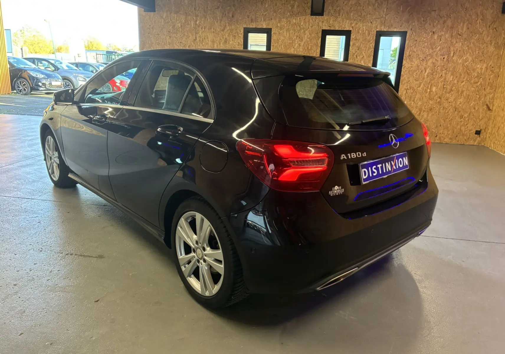 Mercedes Classe A 180 CDI noir vue 3/4 arrière droit en intérieur, feux arrière allumés et jantes argentées visibles.