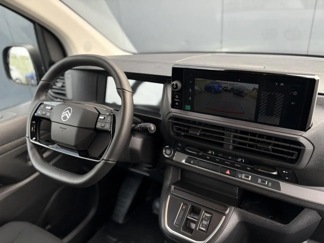 Vue intérieure côté conducteur du tableau de bord du Citroën Jumpy gris, avec écran tactile et volant cuir multifonction.