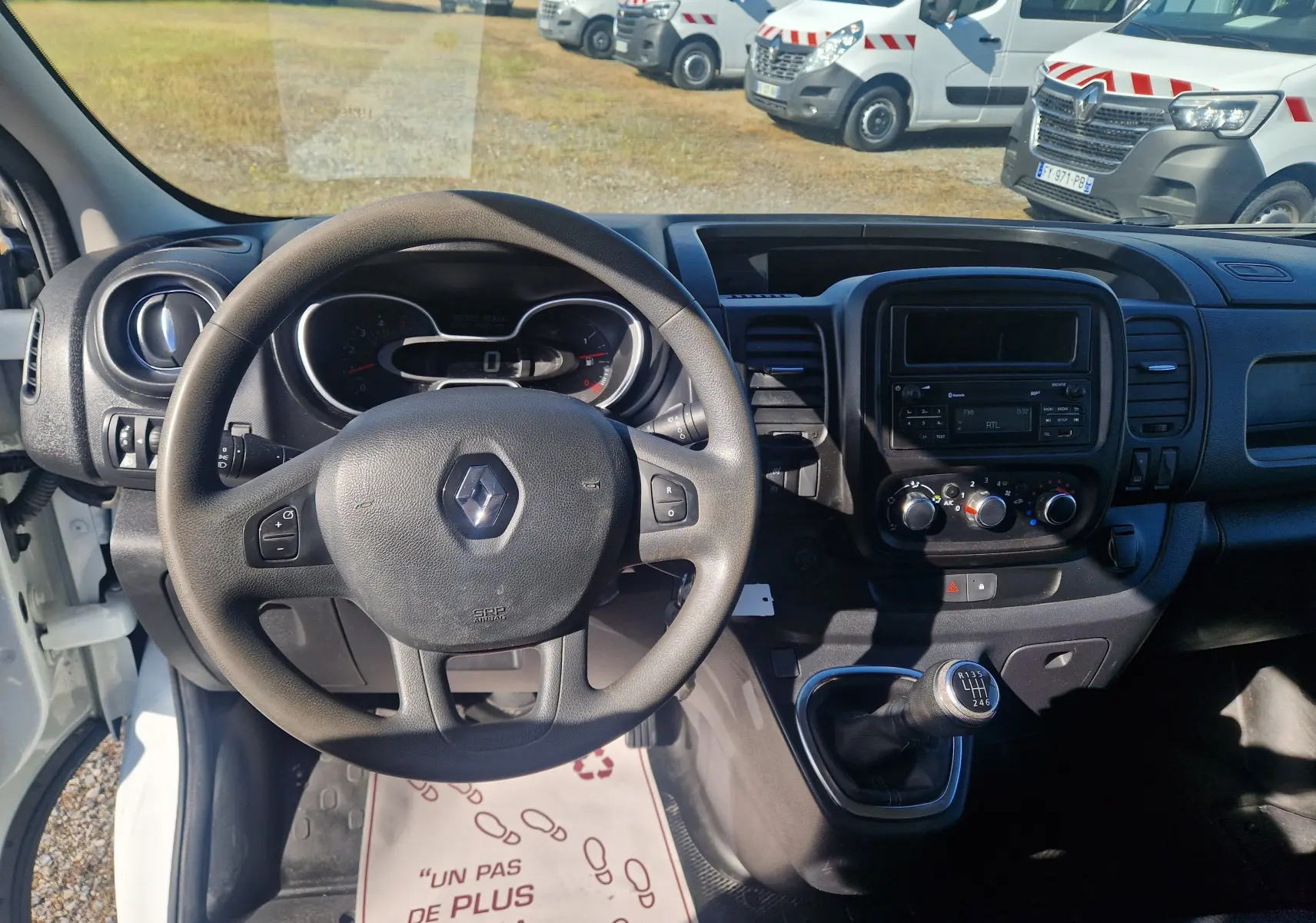 Vue intérieure du tableau de bord et volant noir du Renault Trafic Fourgon blanc, avec levier de vitesse manuel visible.