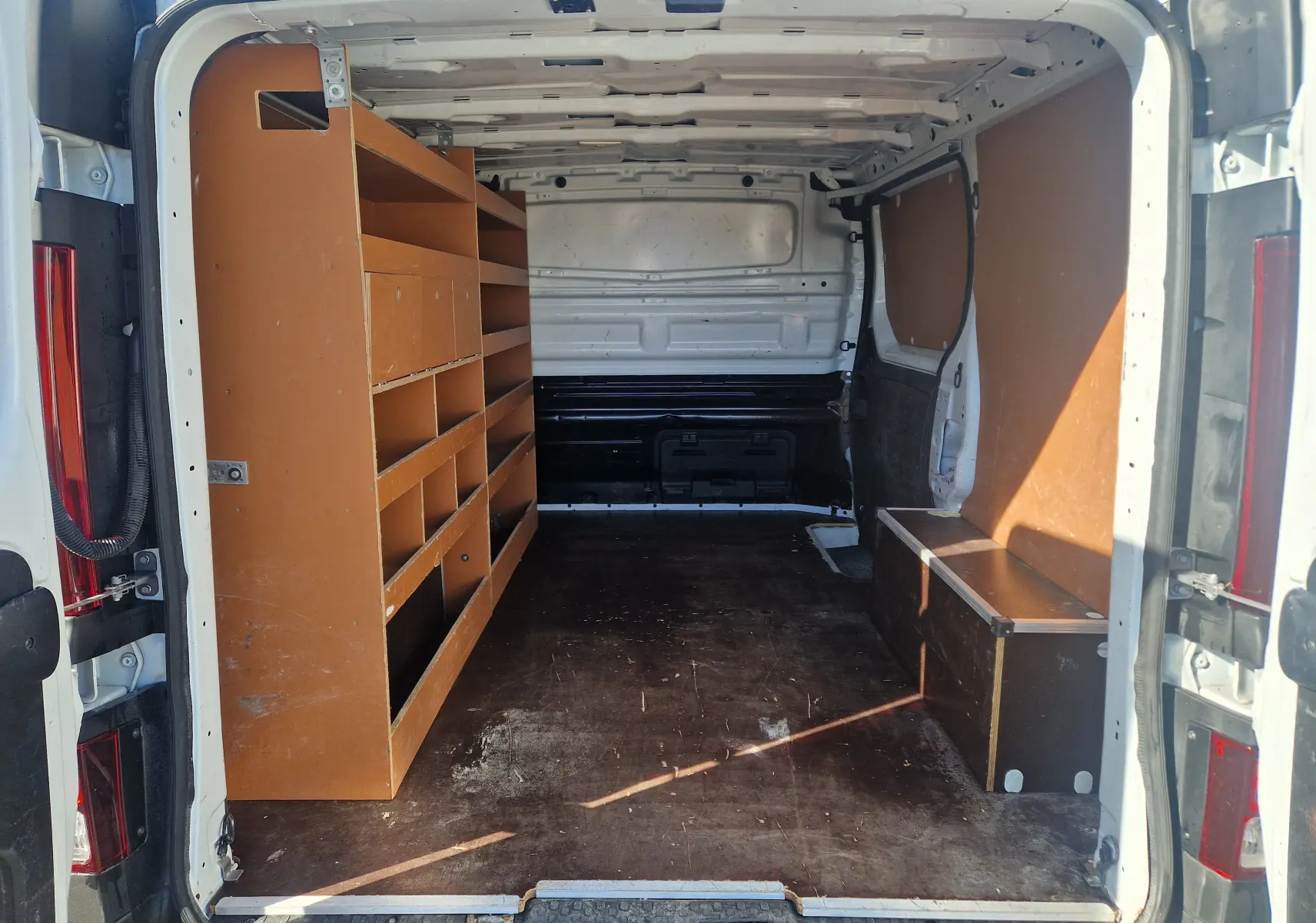 Intérieur du Renault Trafic Fourgon blanc vu de l'arrière, avec aménagements en bois sur les côtés.