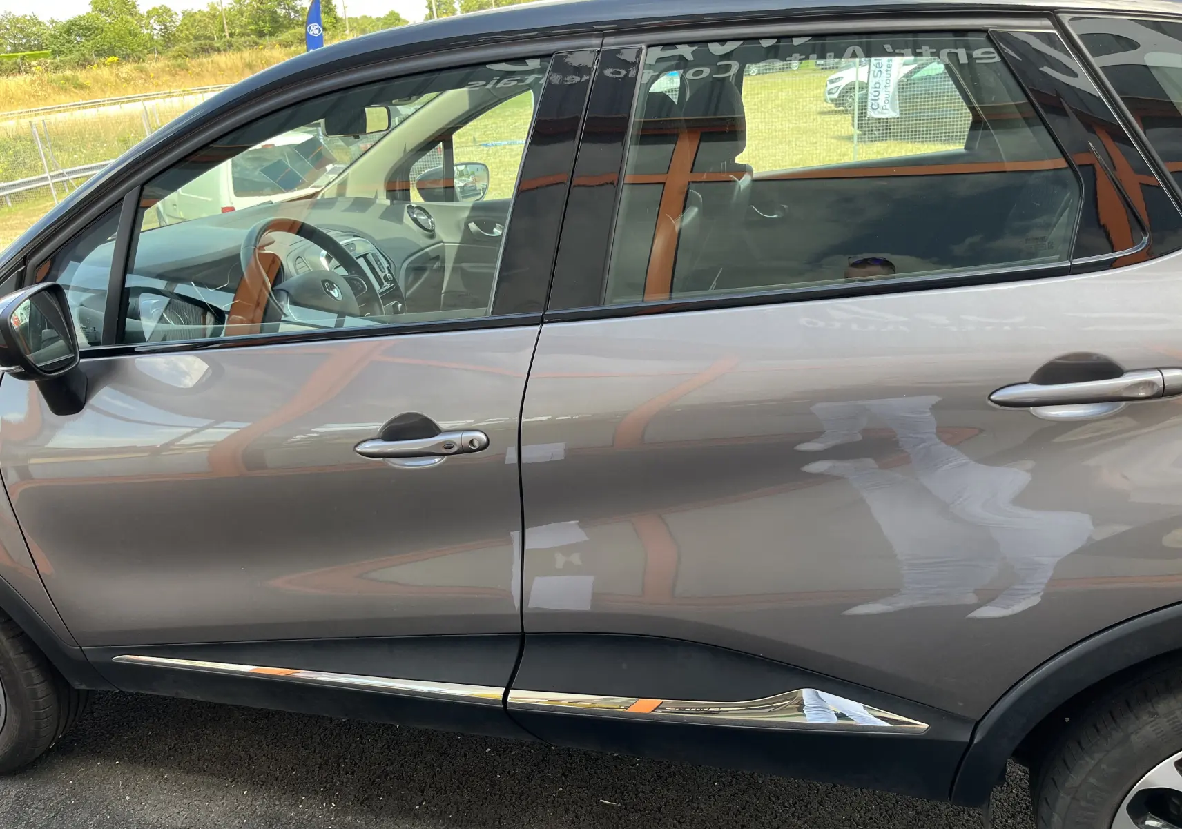 Vue latérale gauche d'un Renault Captur gris 2019 avec détails chromés sur les bas de porte et intérieur visible.