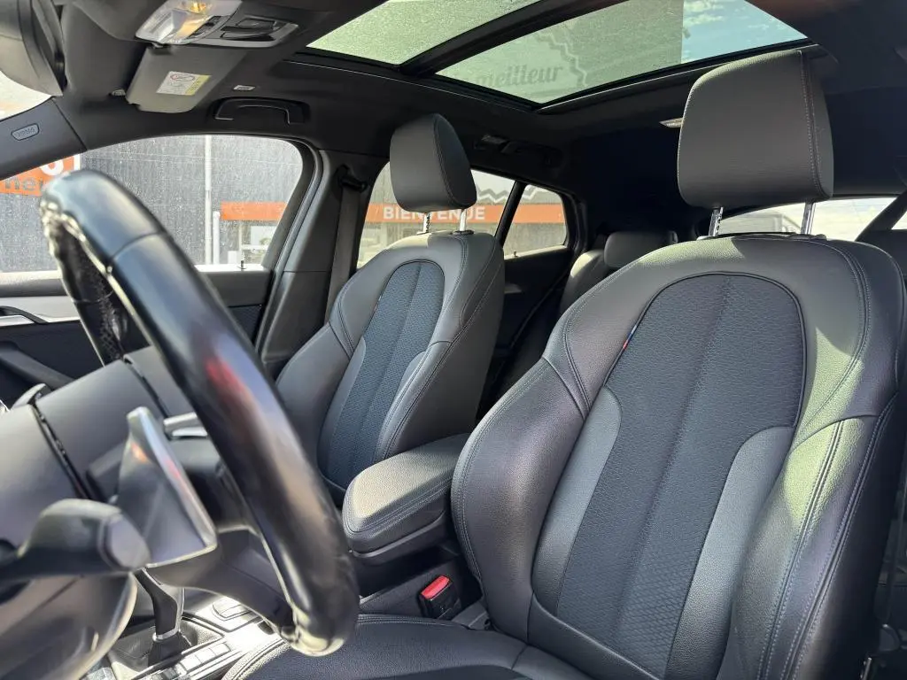 Vue intérieure du BMW X2 M Sport 2021 montrant sièges avant en cuir noir et toit ouvrant panoramique en verre.