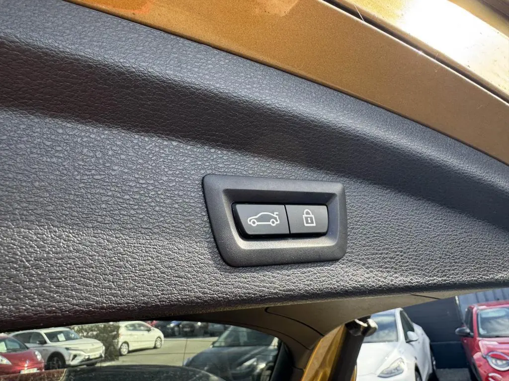 Gros plan sur les boutons d'ouverture et de verrouillage du hayon du BMW X2 jaune, vue intérieure arrière du coffre.