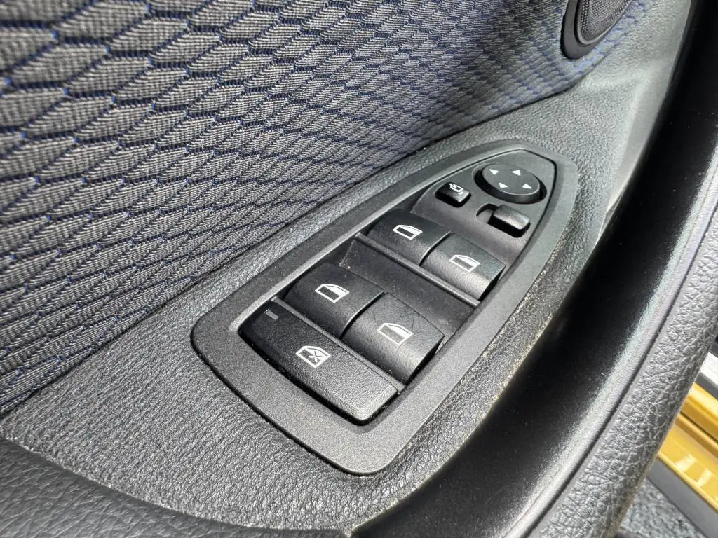 Gros plan sur les commandes des vitres électriques côté conducteur d'une BMW X2 jaune 2021, finition M Sport.