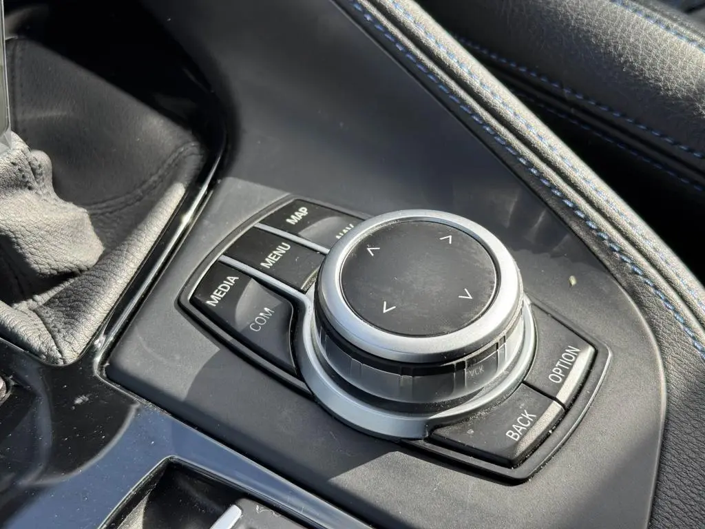 Gros plan sur la molette de commande iDrive entourée de boutons dans la console centrale en cuir noir avec surpiqûres bleues du BMW X2 jaune 2021.