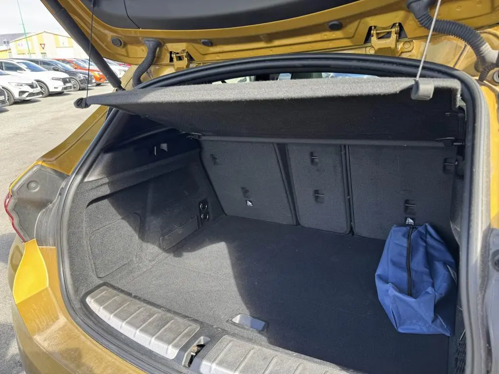 Coffre ouvert vu de l'arrière d'un BMW X2 jaune 2021 avec cache-bagages et sac bleu à droite.