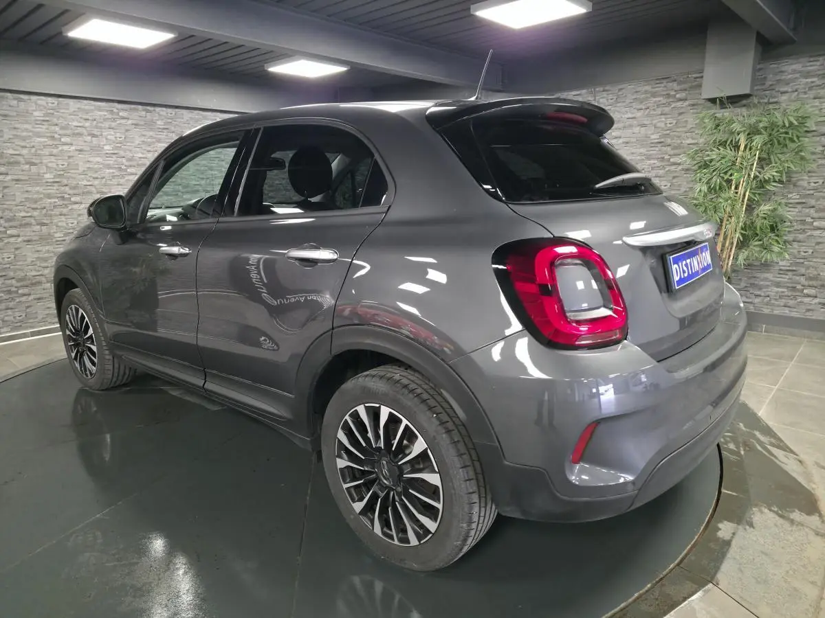Fiat 500X gris vue 3/4 arrière droit, jantes alliage 17'', feux arrière LED, dans un showroom intérieur.