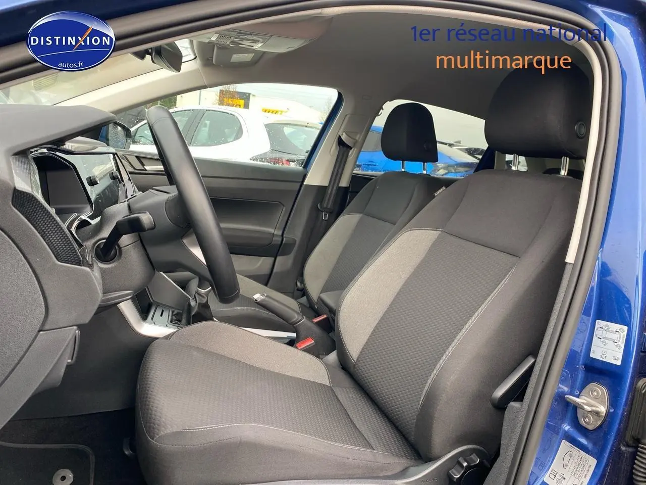 Vue intérieure côté conducteur de la Volkswagen Polo bleu récif, montrant les sièges tissu noir et gris et le volant cuir multifonction.