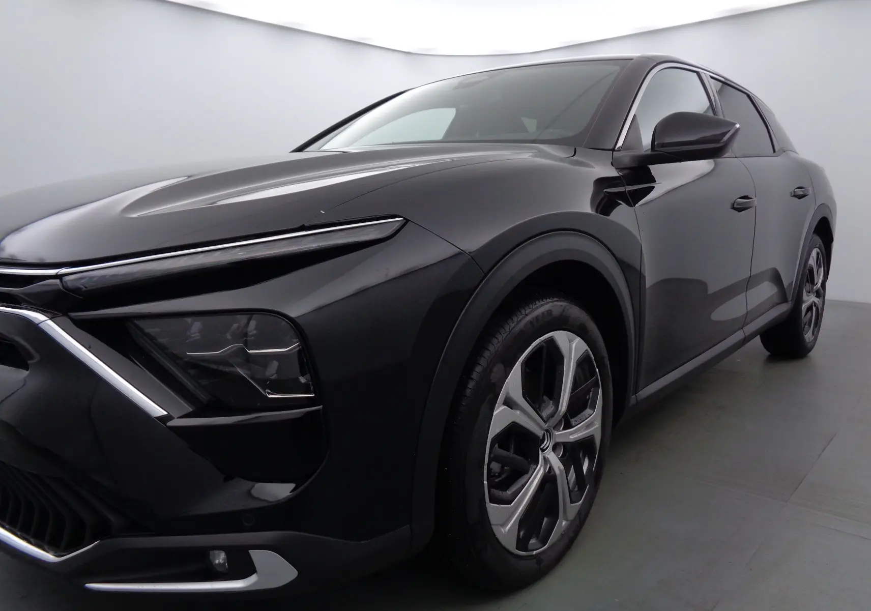 Vue 3/4 avant droit d'une Citroën C5 X noire métal avec phares fins et jantes bi-ton distinctives.