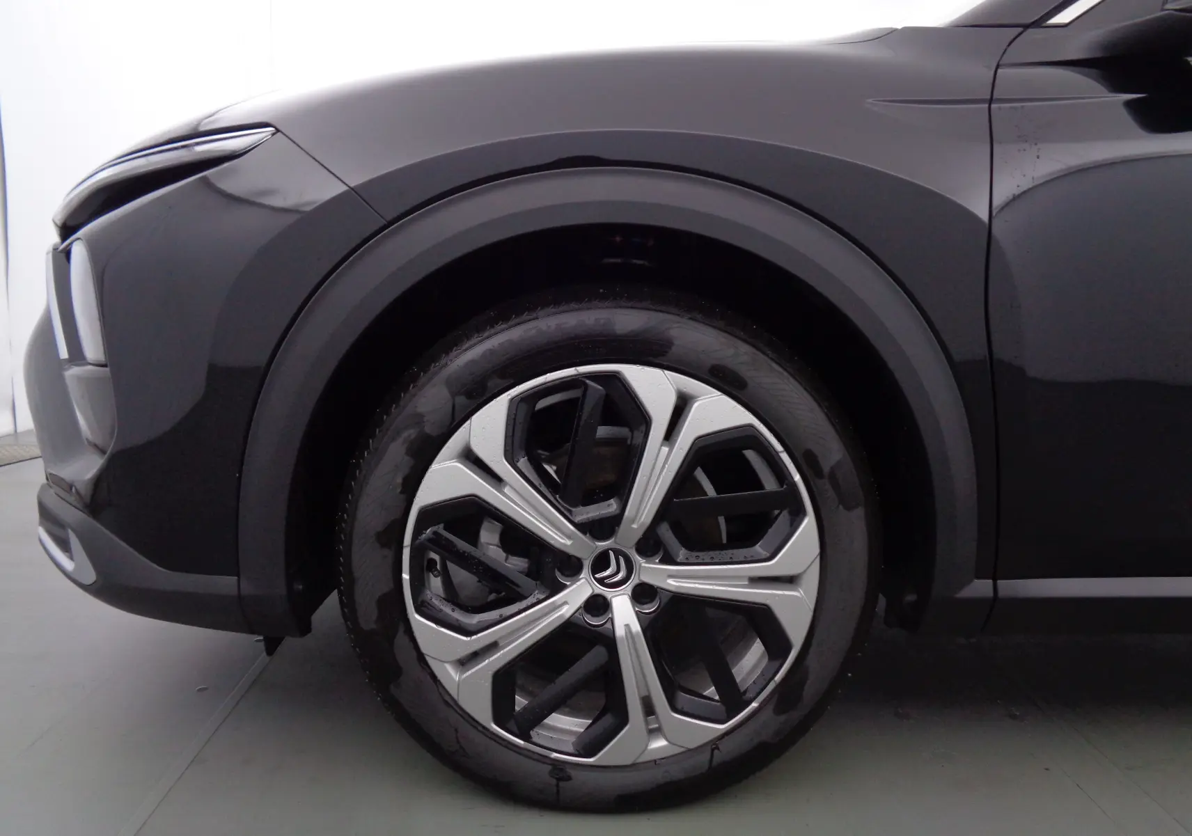 Gros plan sur la roue avant gauche d'une Citroën C5 X noire métal, mettant en valeur la jante bi-ton au design moderne.