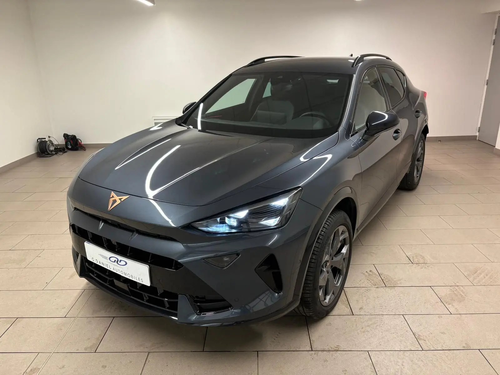 Vue 3/4 avant droit du CUPRA Formentor gris magnétique avec phares allumés et logo cuivré sur le capot.