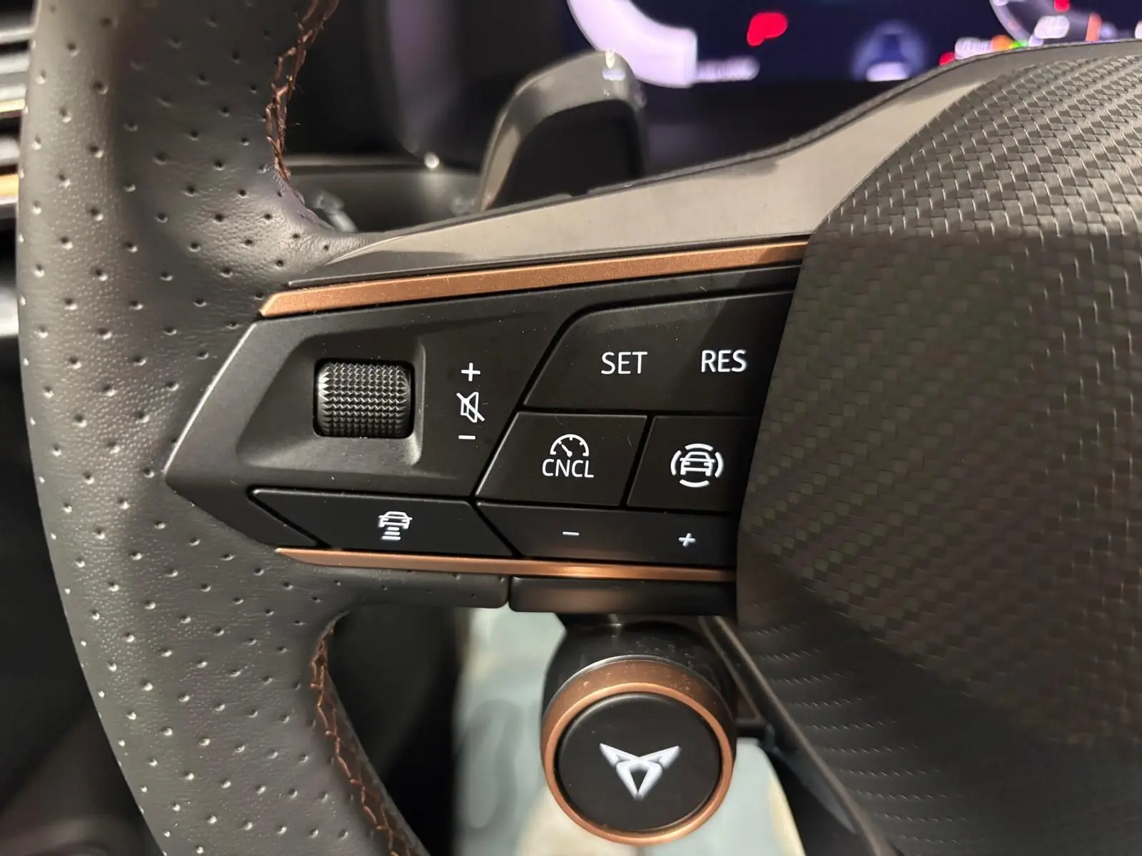 Gros plan sur les commandes du volant perforé avec logo CUPRA, soulignant les fonctions d'assistance à la conduite.