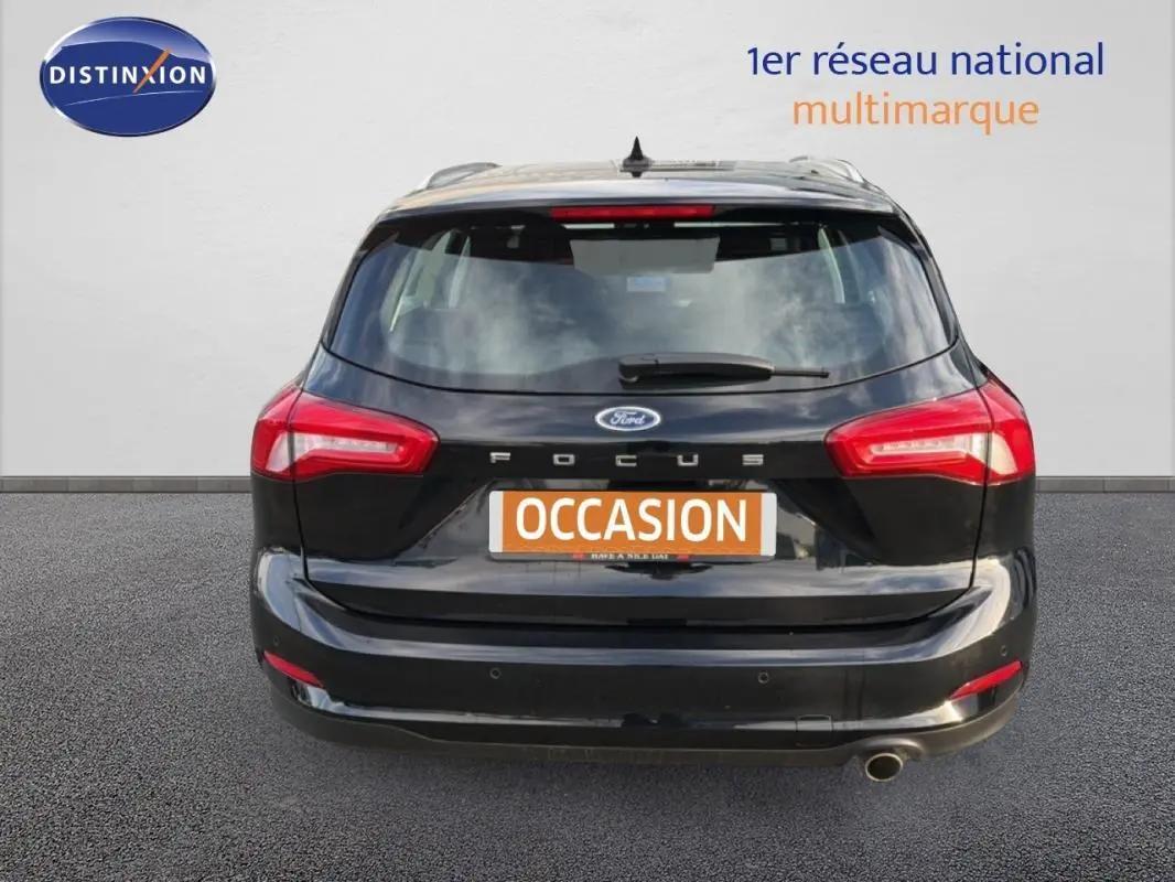 Vue arrière d'une Ford Focus SW noire de 2019 avec barres de toit et feux arrière allumés.