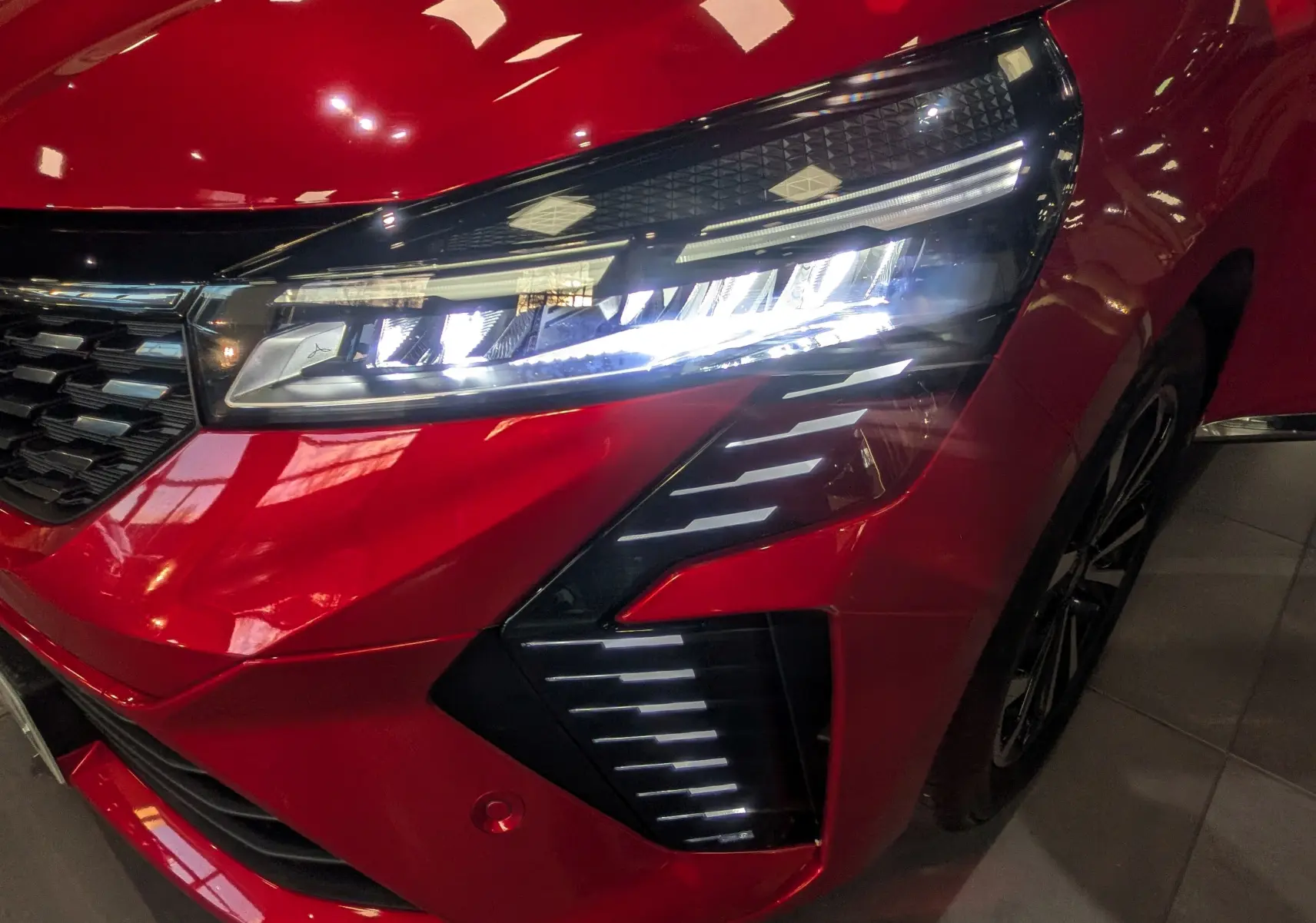 Gros plan sur le phare avant droit allumé d’une Renault Clio V rouge flamme, soulignant la calandre et les feux LED distinctifs.