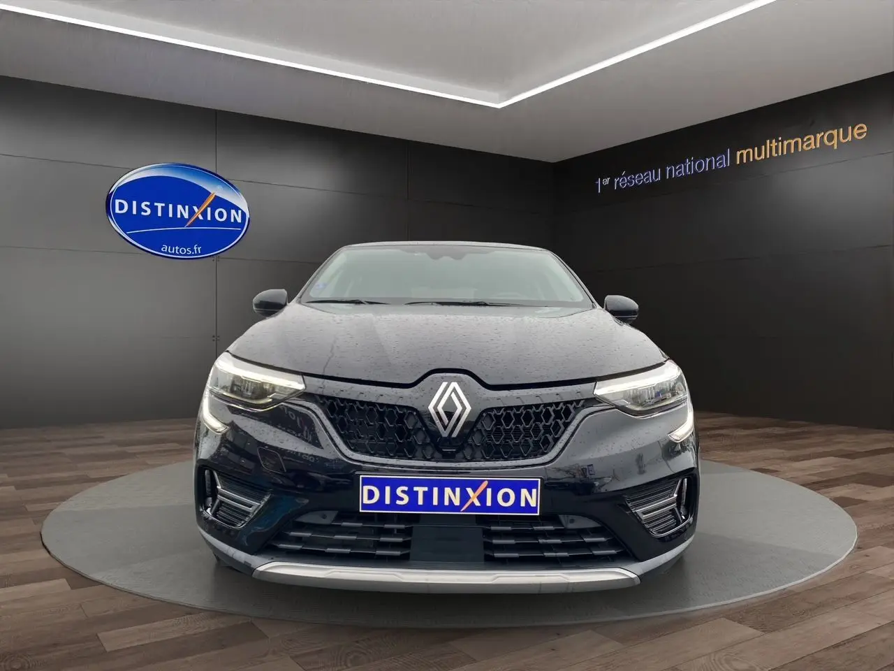 Vue avant d'un Renault Arkana noir 2024 avec calandre hexagonale et phares LED allumés en intérieur showroom.