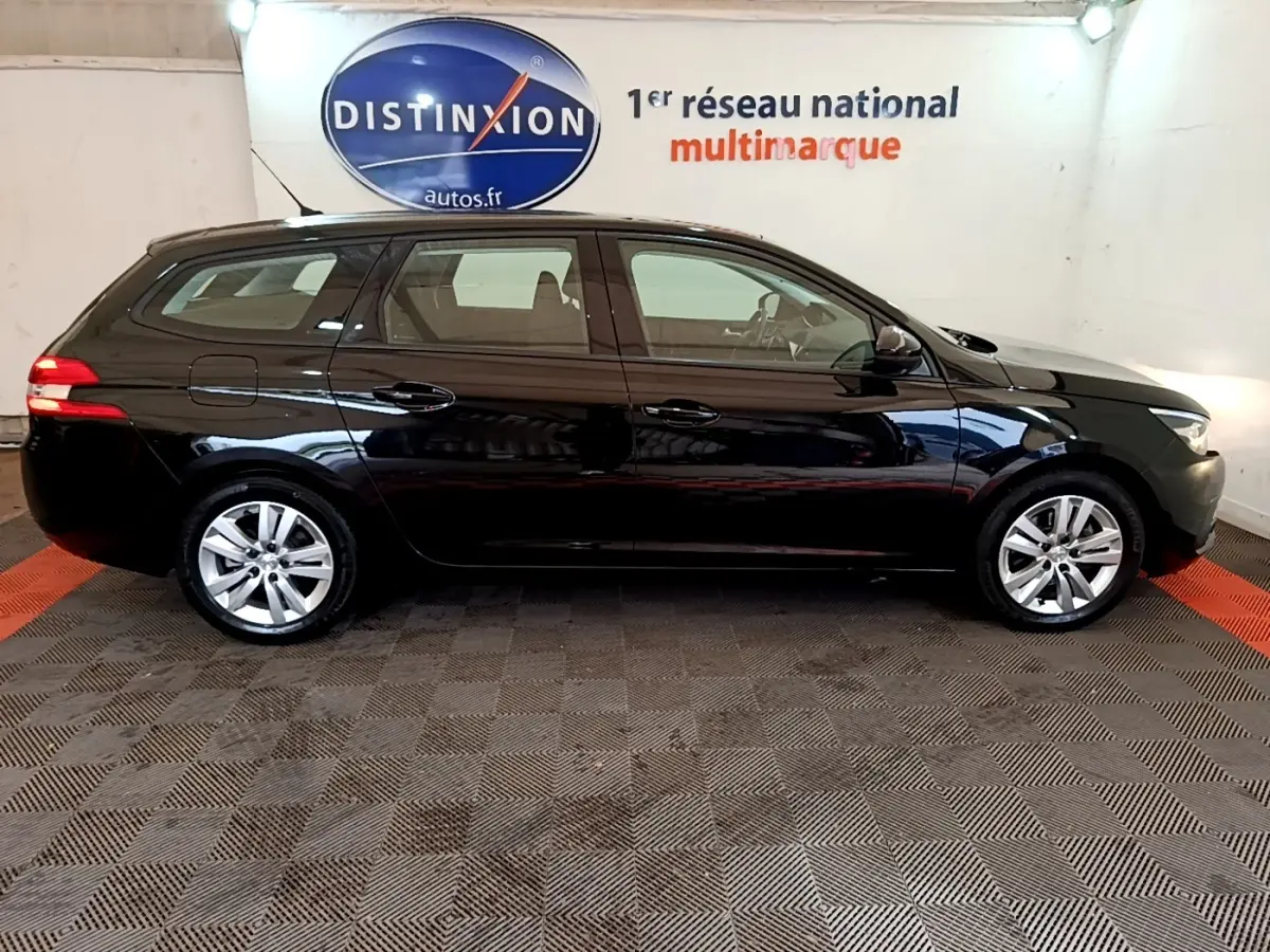 Peugeot 308 break noir vue de profil côté gauche, stationnée en intérieur avec logo Distinxion en arrière-plan.