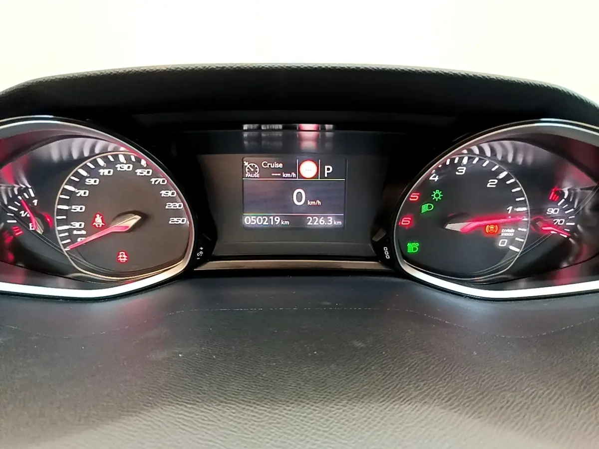 Vue rapprochée du tableau de bord numérique de la Peugeot 308 noir, affichant la vitesse à 0 km/h et divers voyants allumés.