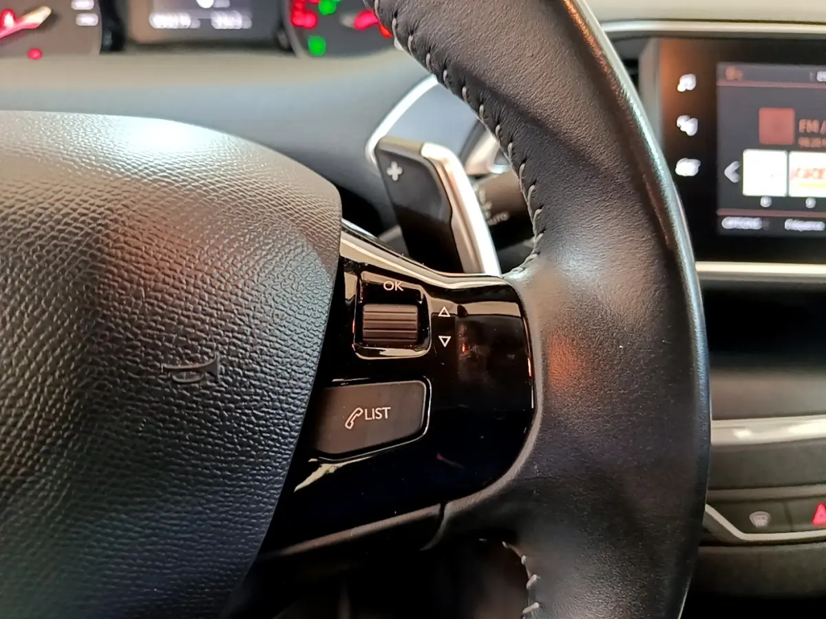 Gros plan sur le volant cuir noir de la Peugeot 308 2020 avec commandes intégrées et écran tactile en arrière-plan.