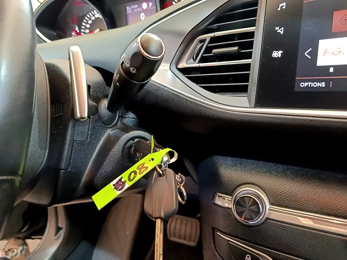 Vue rapprochée de l’intérieur noir de la Peugeot 308, montrant le volant, la clé dans le contact et l’écran tactile.