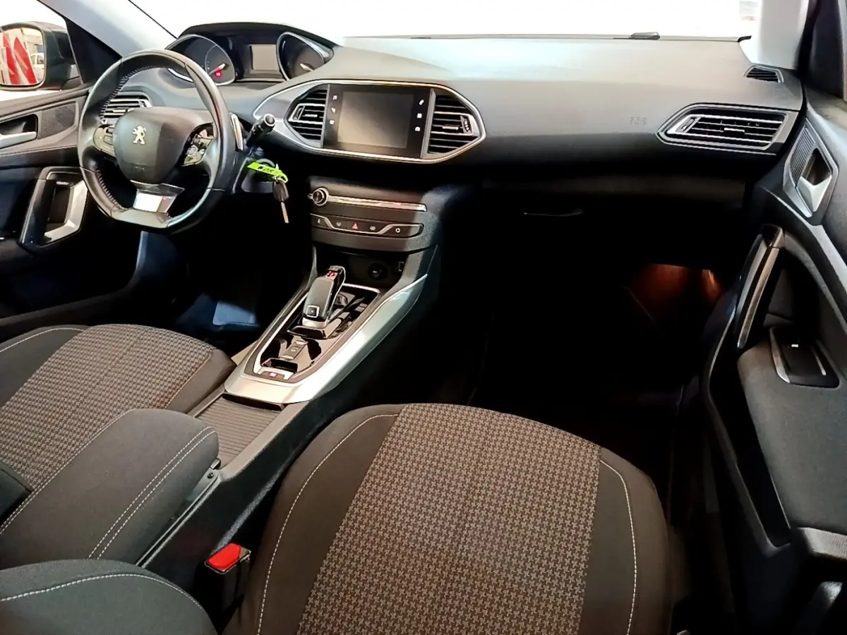 Vue intérieure avant droite de la Peugeot 308 noire, montrant le tableau de bord avec écran tactile et volant cuir multifonctions.