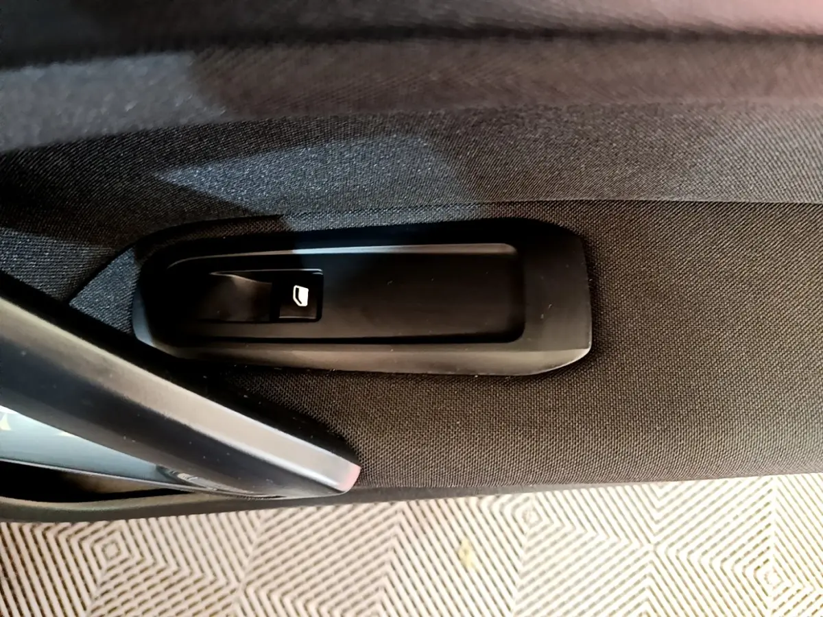 Gros plan sur la commande d’ouverture de coffre intégrée à la garniture intérieure noire d’une Peugeot 308.