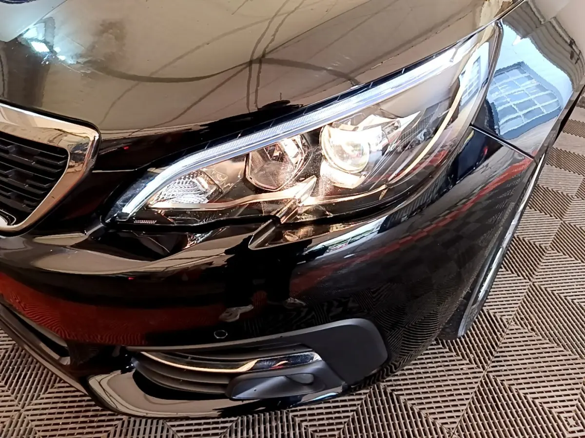 Gros plan sur le phare avant droit d'une Peugeot 308 noire, mettant en valeur les feux à LED et la calandre brillante.