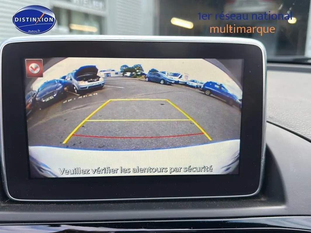 Écran tactile montrant la caméra de recul d'une Fiat 124 Spider blanche, vue arrière avec lignes de guidage colorées.