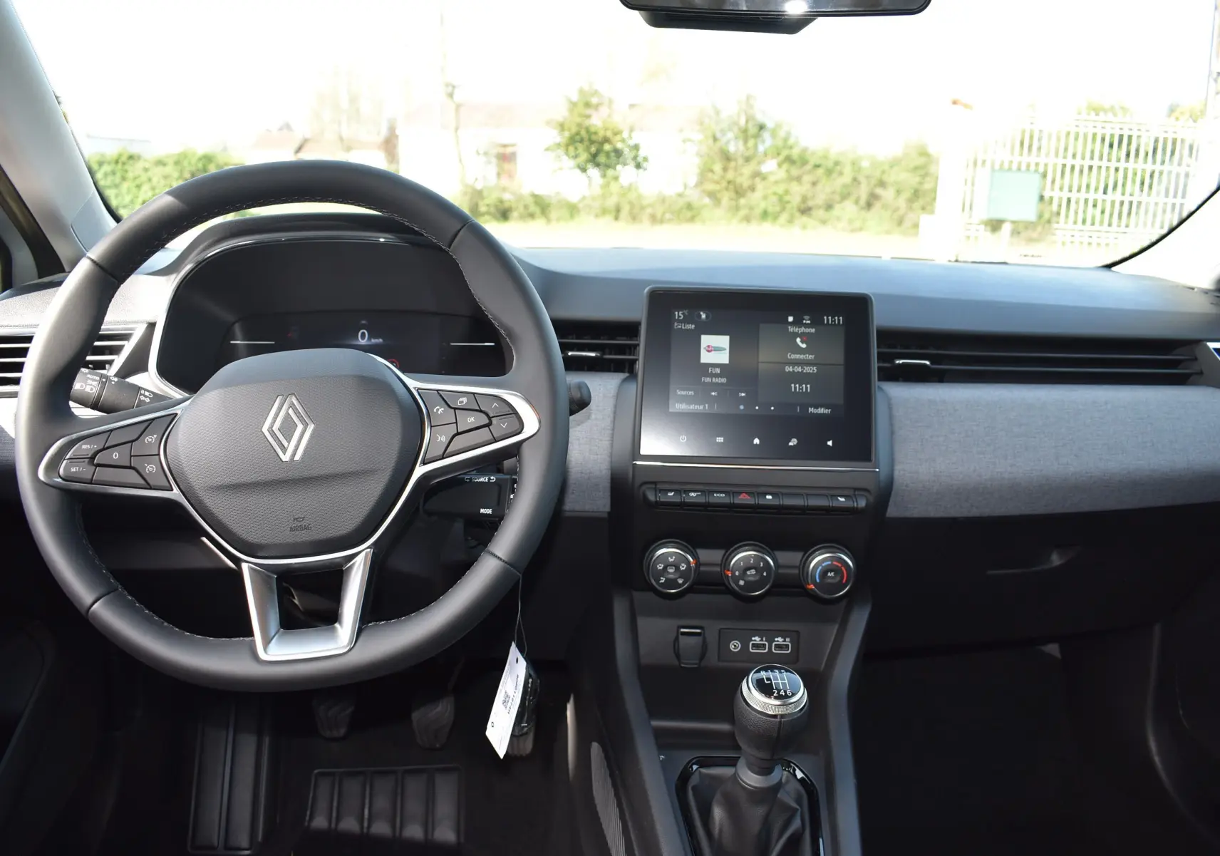 Intérieur de la Renault Clio V TCE 90 gris, vue de face sur le volant, tableau de bord et levier de vitesse manuel.