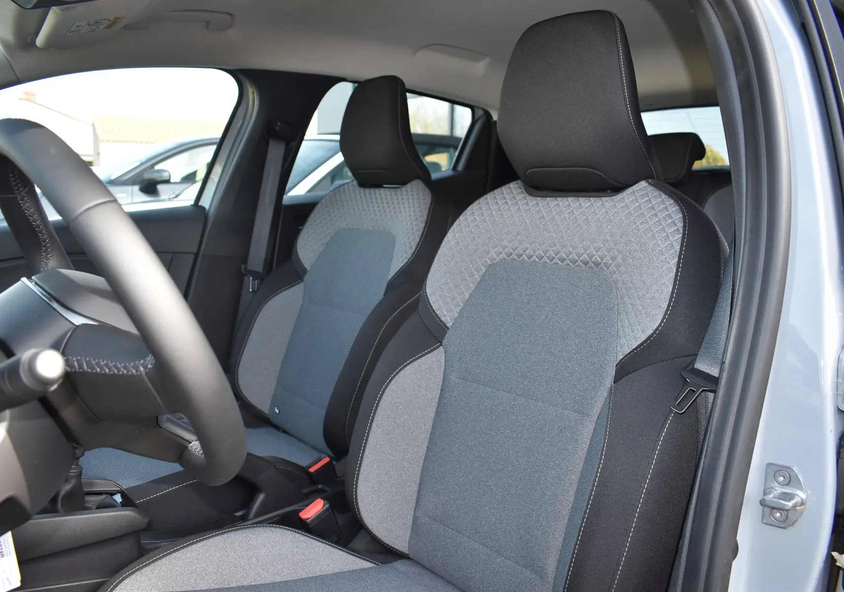 Vue intérieure de la Renault Clio V TCE 90 gris, mettant en valeur les sièges avant en tissu bicolore gris et noir.