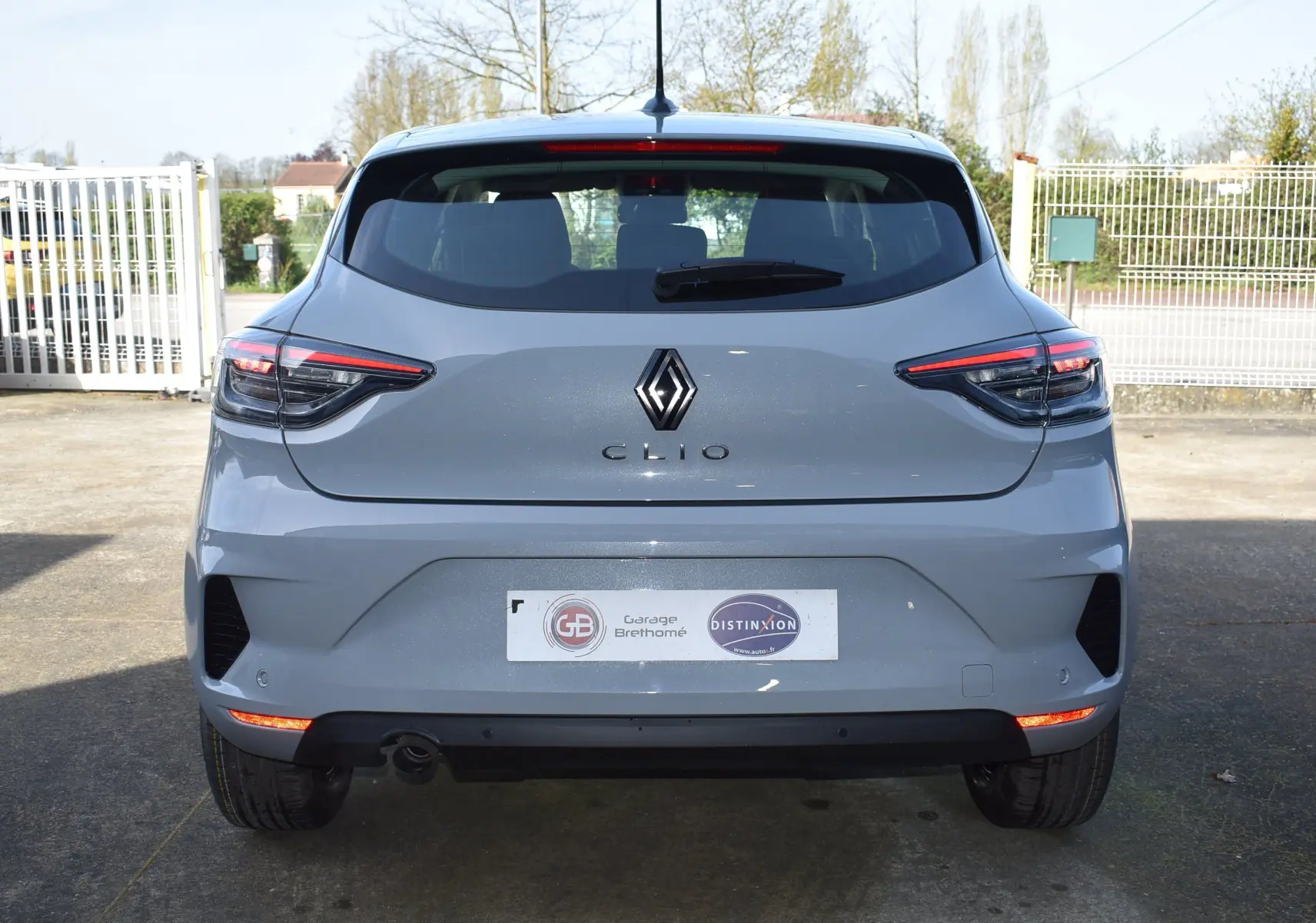 Vue arrière d'une Renault Clio V gris 2024 avec feux LED et logo Renault bien visibles sur un parking extérieur.
