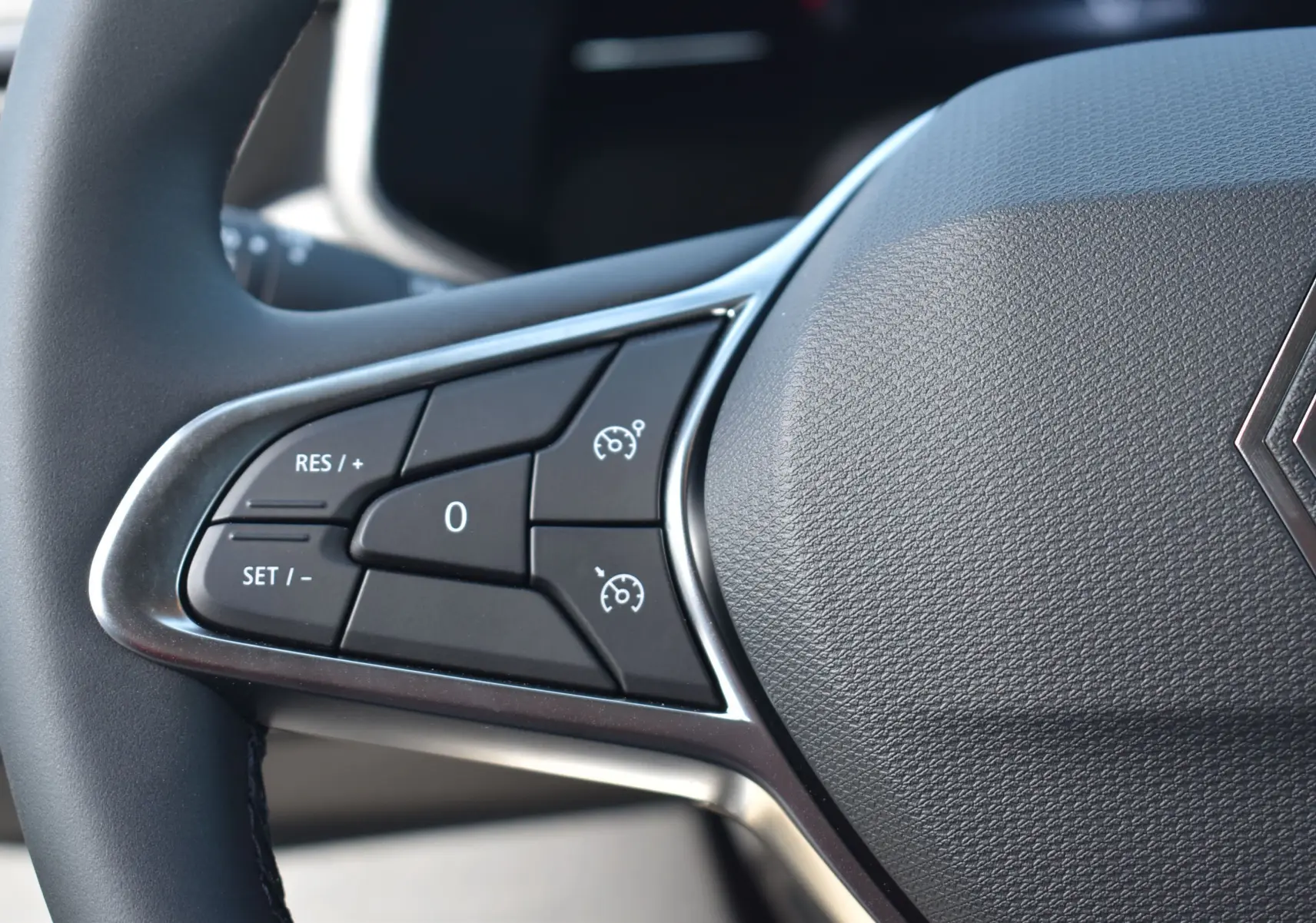 Gros plan sur les commandes de régulateur de vitesse à gauche du volant gris texturé d'une Renault Clio V 2024.