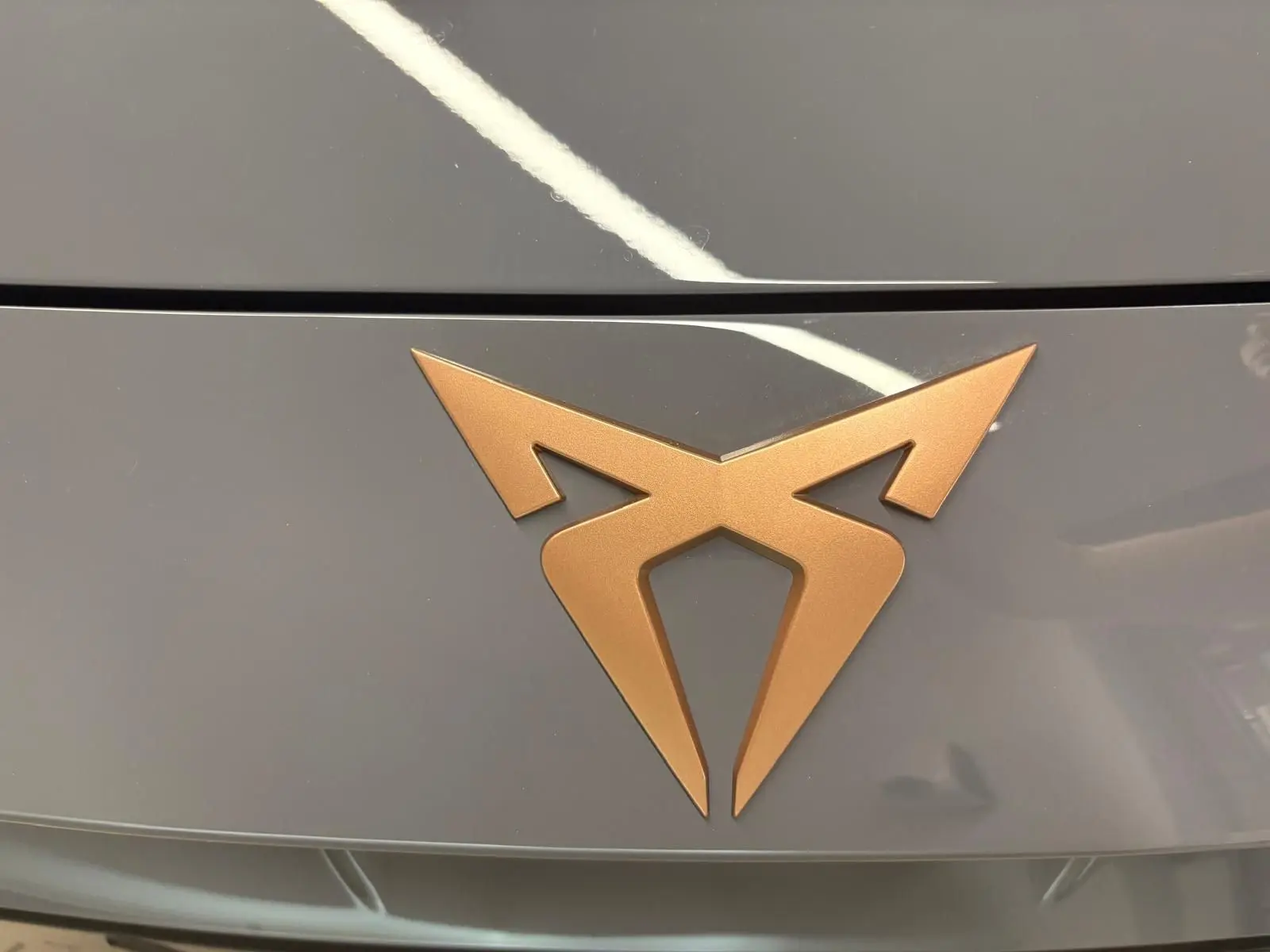 Gros plan sur le logo CUPRA bronze sur le capot gris graphène du Formentor 2025 avec toit ouvrant panoramique.