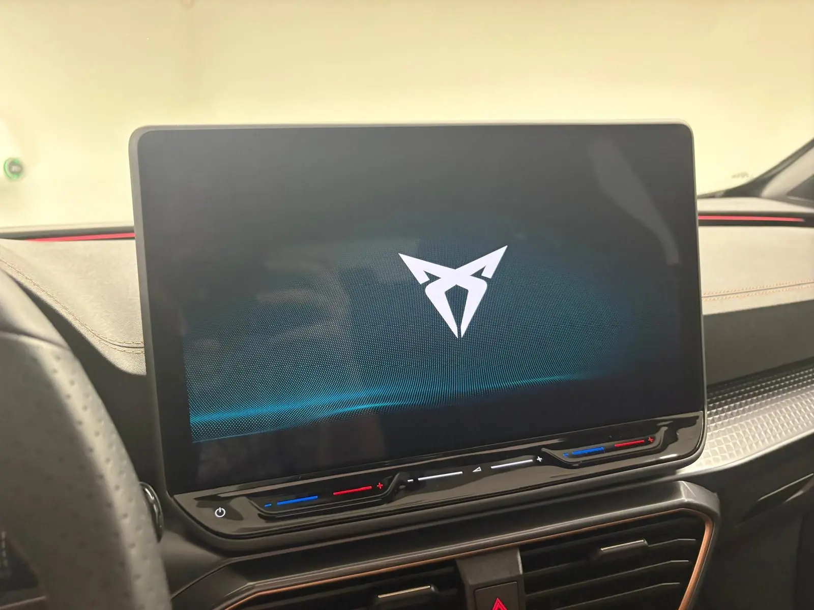 Écran tactile central allumé avec logo CUPRA, tableau de bord noir et surpiqûres orange dans l'habitacle du Formentor.